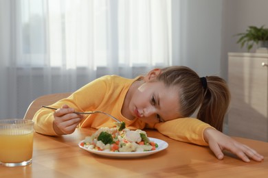 Cute little girl refusing to eat vegetable salad at home