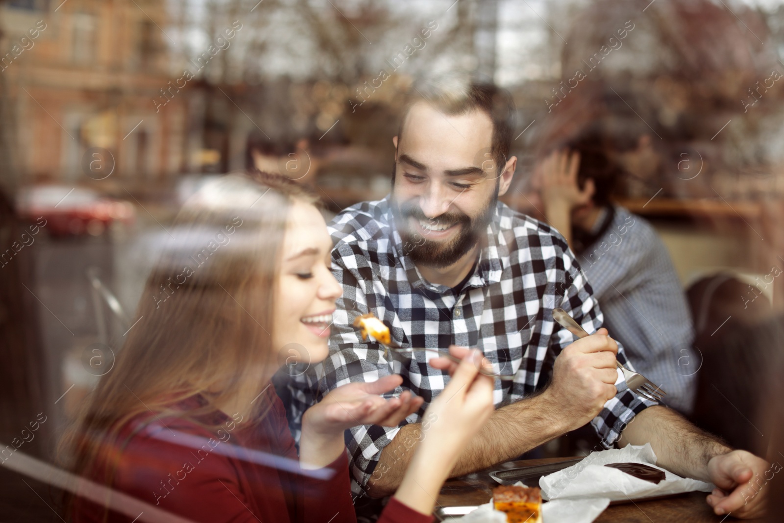 Photo of Lovely young couple spending time together in cafe, view from outdoors through window