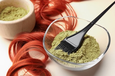 Photo of Bowlhenna powder, brush and red strand on beige background, closeup. Natural hair coloring