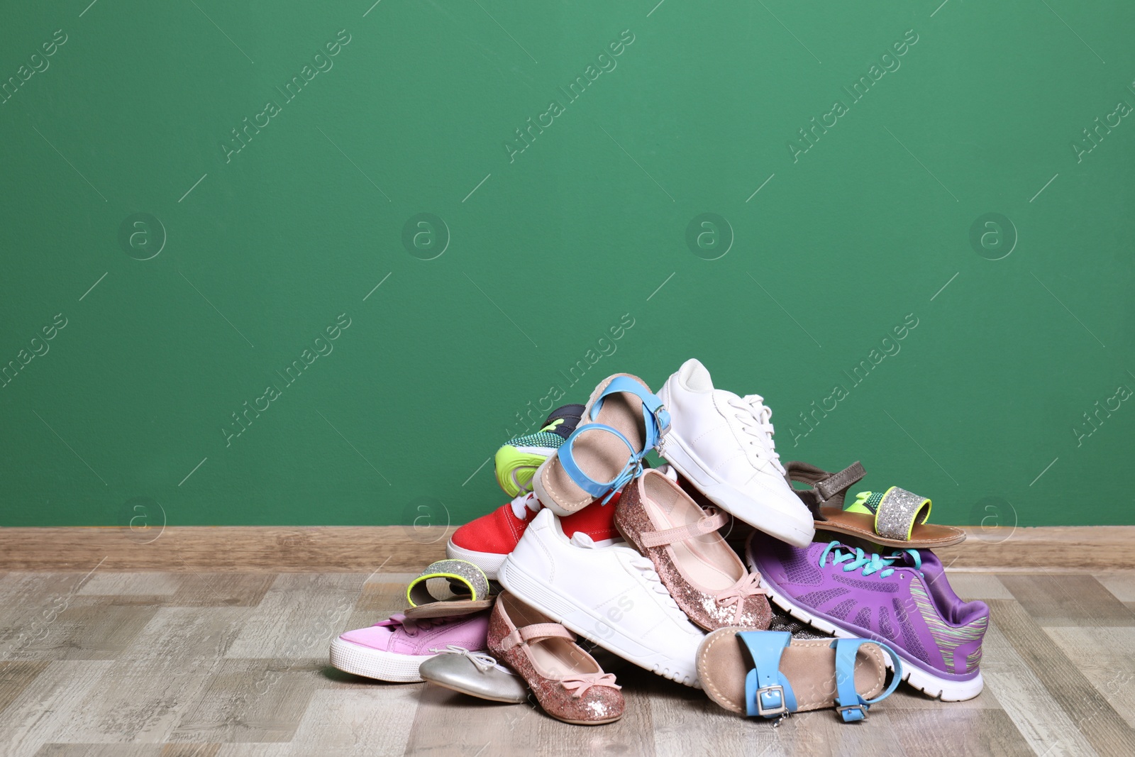 Photo of Heap of different shoes on floor against color wall. Space for text