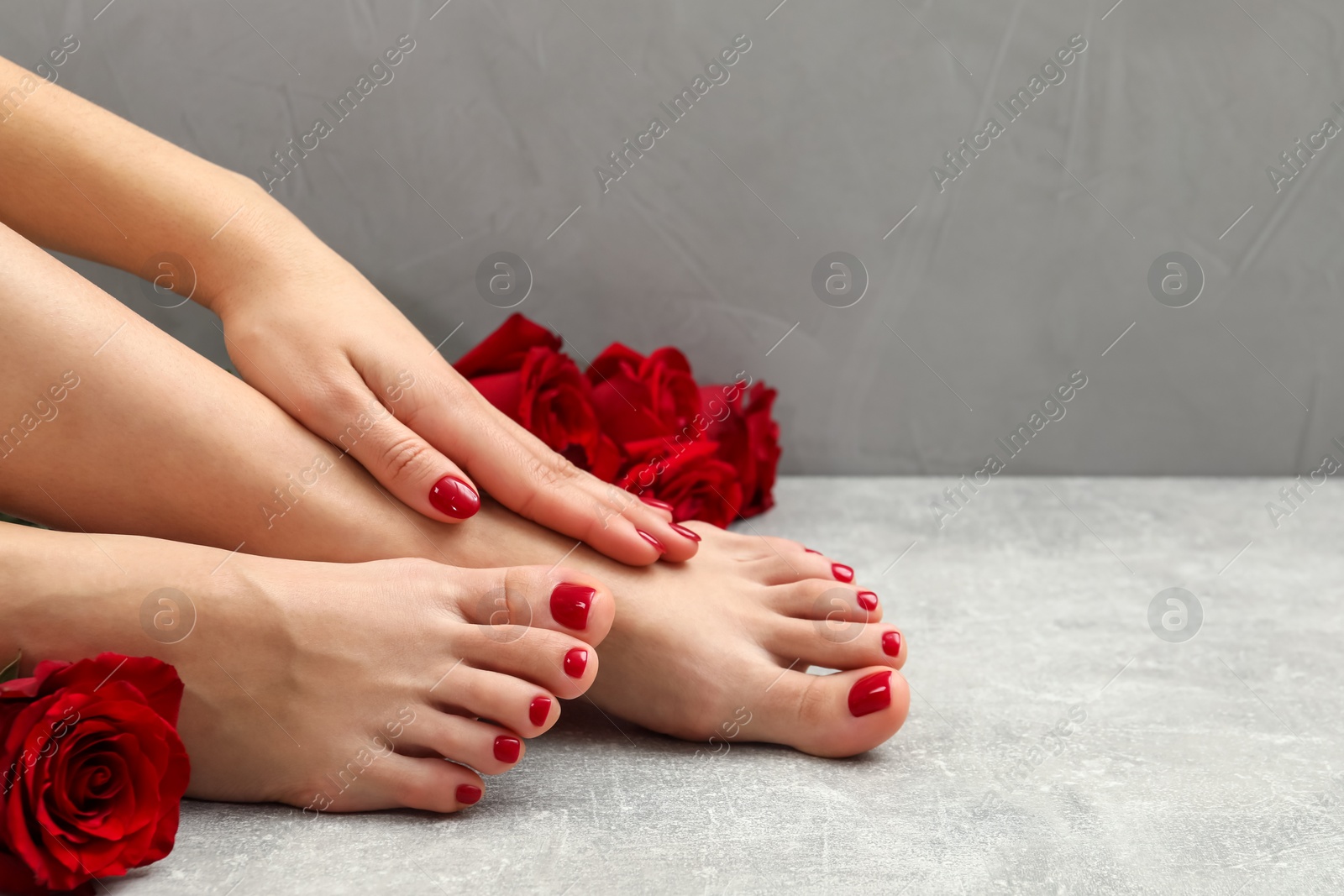 Photo of Woman with stylish red toenails after pedicure procedure and rose flowers on grey textured floor, closeup. Space for text