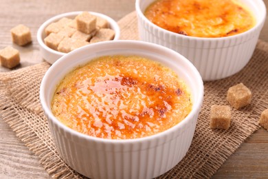 Delicious creme brulee in bowls and sugar cubes on wooden table, closeup