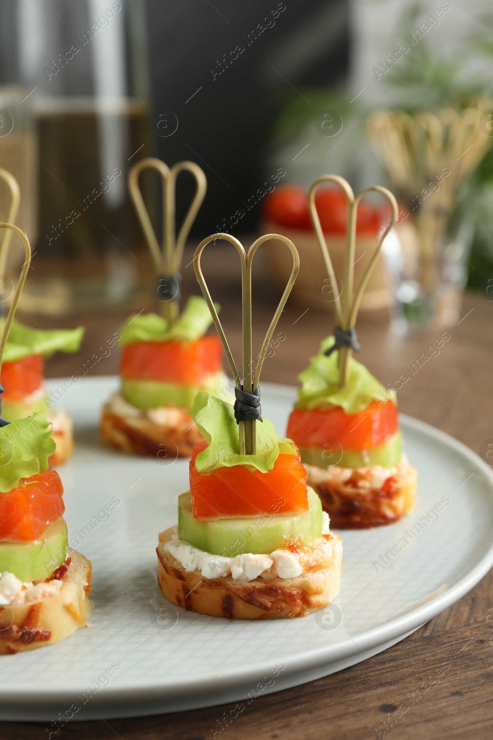 Photo of Tasty canapes with salmon, cucumber, bread and cream cheese on wooden table, closeup