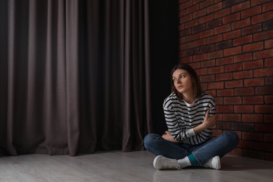 Sad young woman sitting on floor indoors, space for text