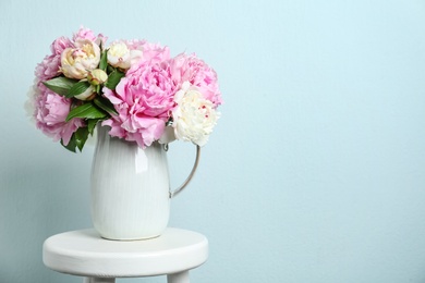 Photo of Beautiful peonies in jug on white stool against light blue background. Space for text