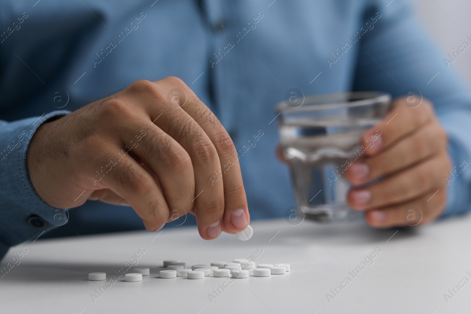 Photo of Man with antidepressant pills and glass of water at white table, closeup