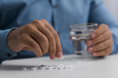 Man with antidepressant pills and glass of water at white table, closeup