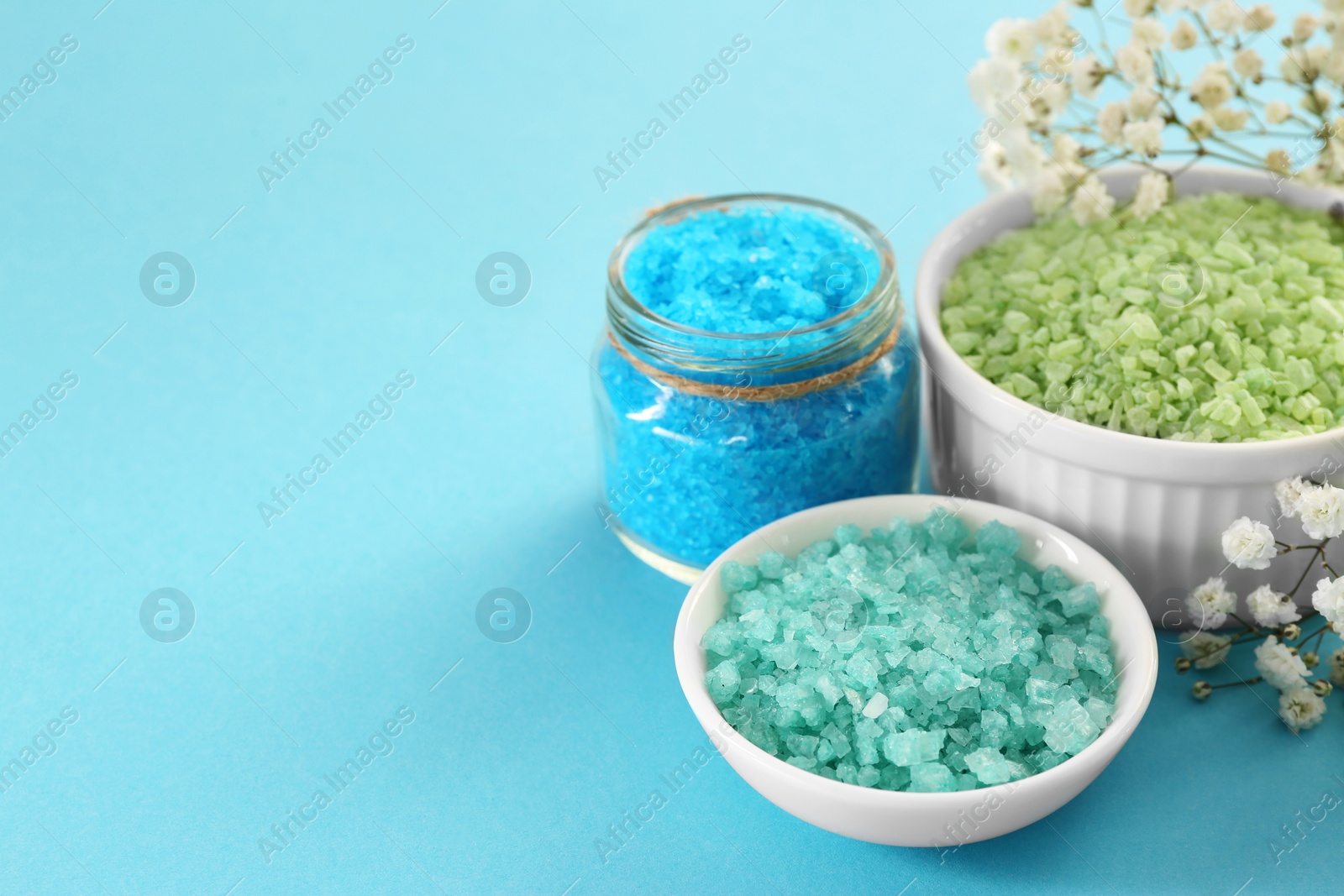 Photo of Aromatic sea salt and beautiful flowers on light blue background. Space for text