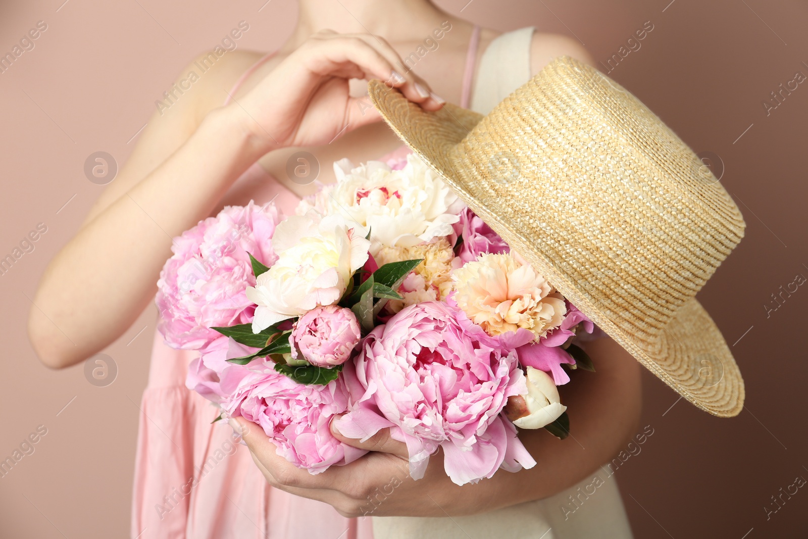 Photo of Woman with bouquet of beautiful peonies in bag and hat on beige background, closeup