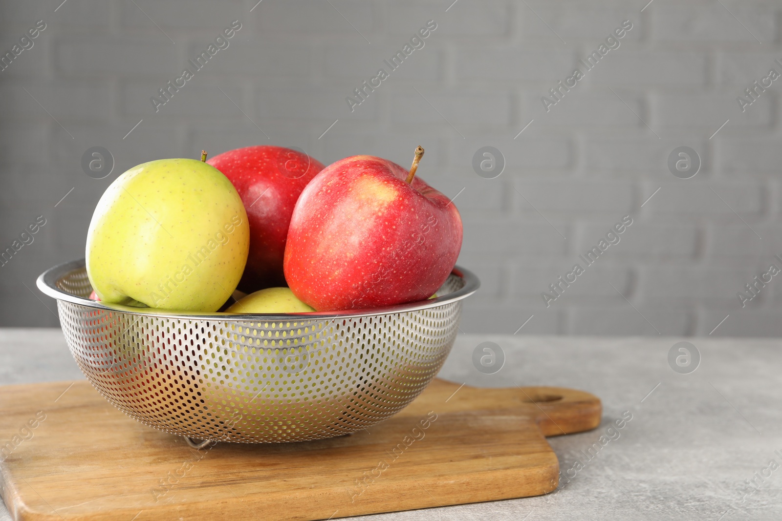 Photo of Fresh ripe apples in colander on light grey table. Space for text