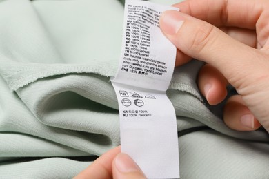 Photo of Woman holding clothing labels on light green garment, closeup
