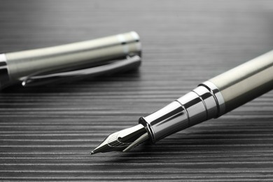 Photo of Stylish silver fountain pen on black wooden table, closeup