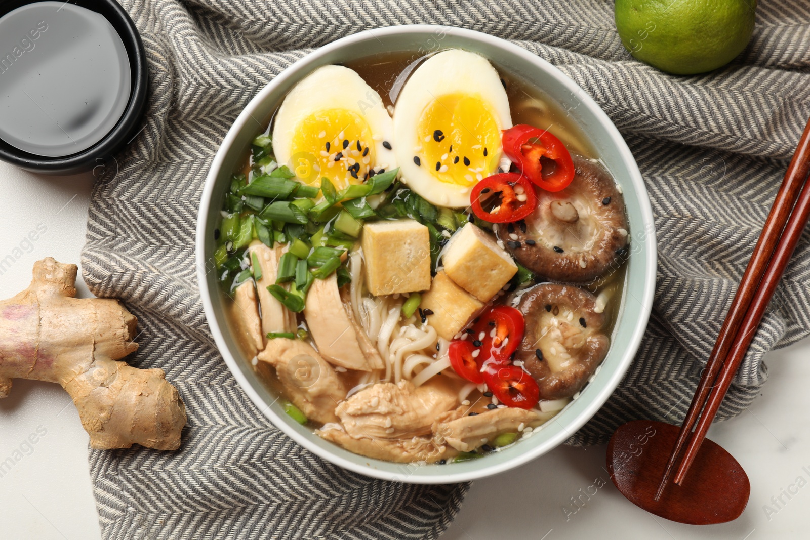 Photo of Bowl of delicious ramen, ingredients and chopsticks on white table, flat lay. Noodle soup