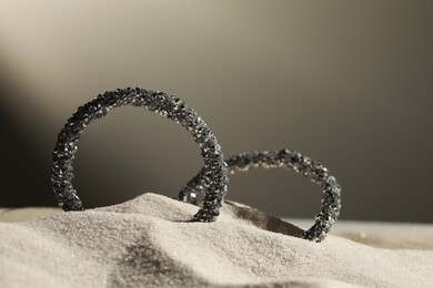 Photo of Luxury jewelry. Stylish presentation of earrings in sand against grey background, closeup