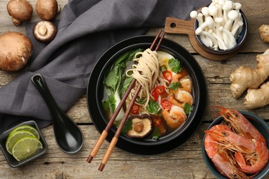 Flat lay composition with delicious ramen in bowl and ingredients on wooden table. Noodle soup