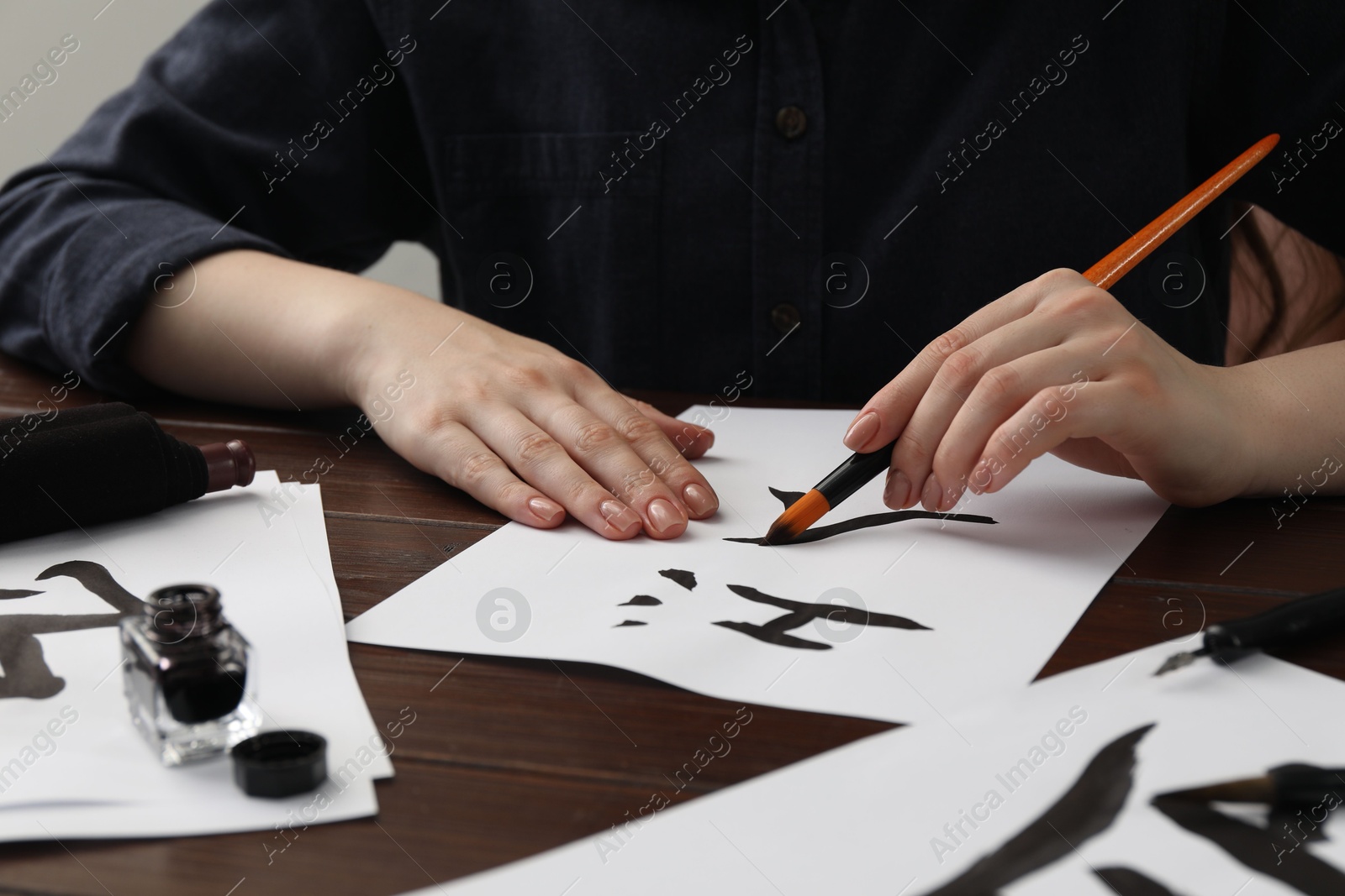 Photo of Calligraphy. Woman with brush and inkwell writing hieroglyphs on paper at wooden table, closeup