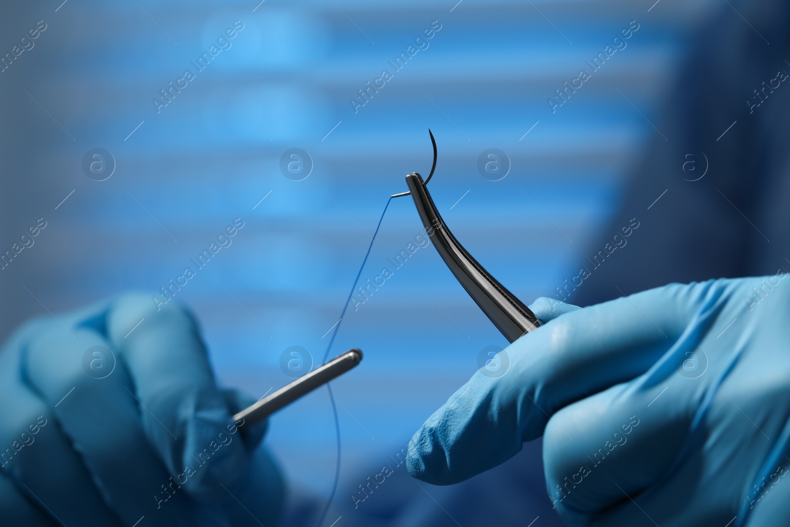 Photo of Professional surgeon holding forceps with suture thread on blurred background, closeup. Medical equipment