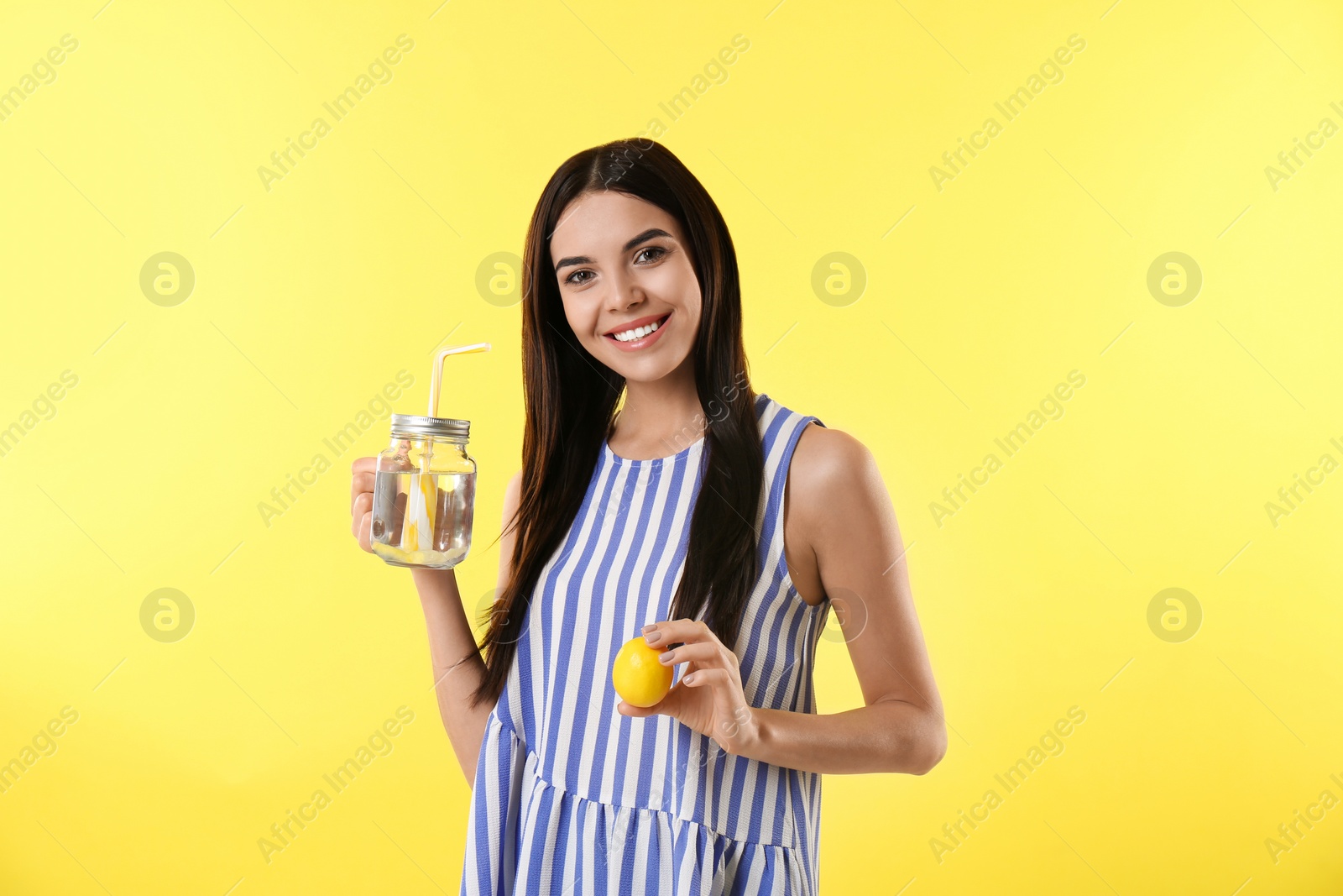 Photo of Beautiful young woman with tasty lemon water and fresh fruit on yellow background