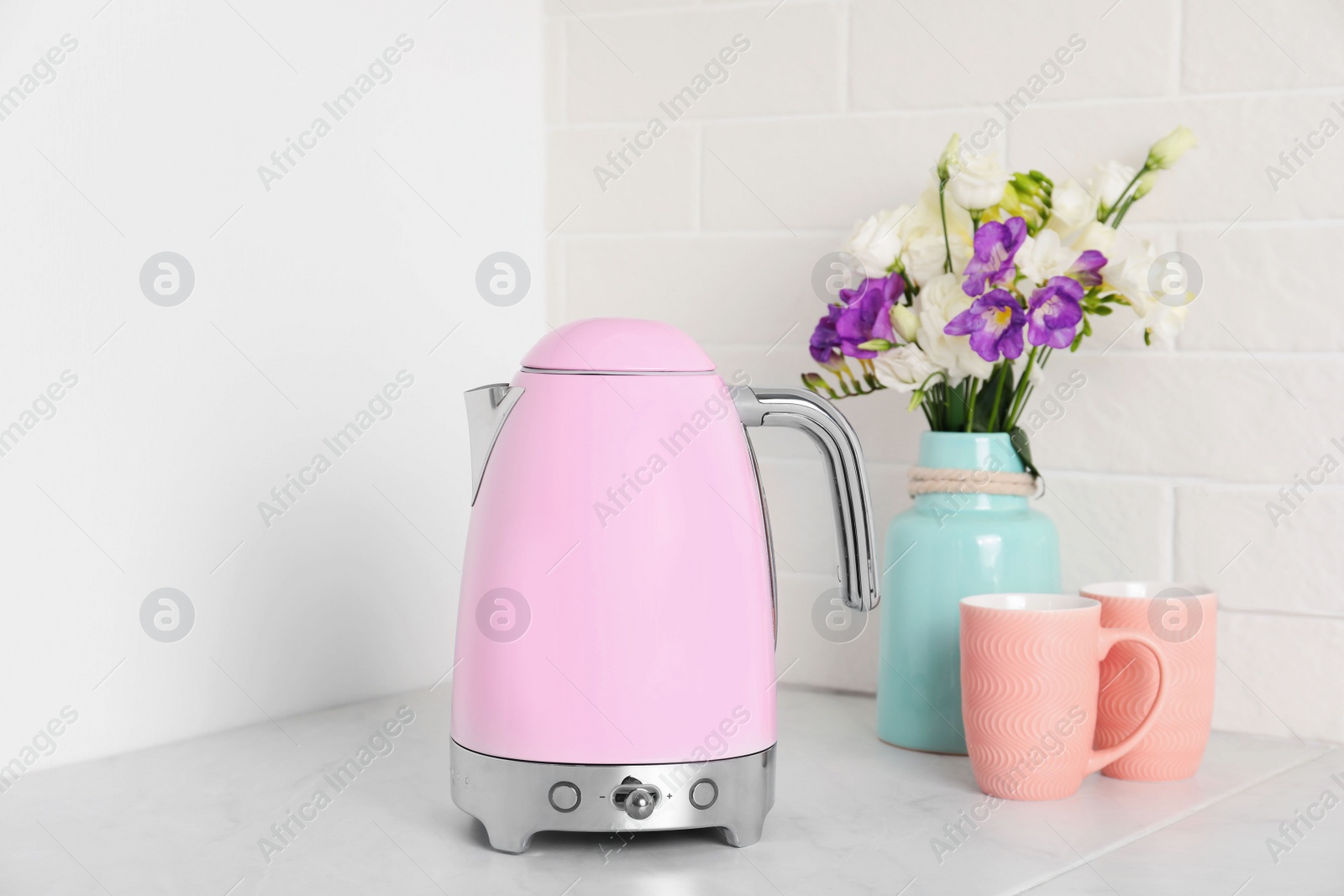 Photo of Modern electric kettle, bouquet and cups on counter in kitchen