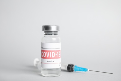 Vial with coronavirus vaccine and syringe on light background