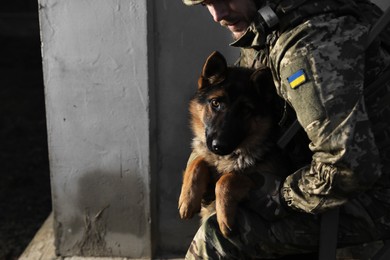 Photo of Ukrainian soldier with German shepherd dog near wall outdoors, closeup. Space for text