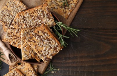 Cereal crackers with flax, sunflower, sesame seeds and rosemary on wooden table, top view. Space for text