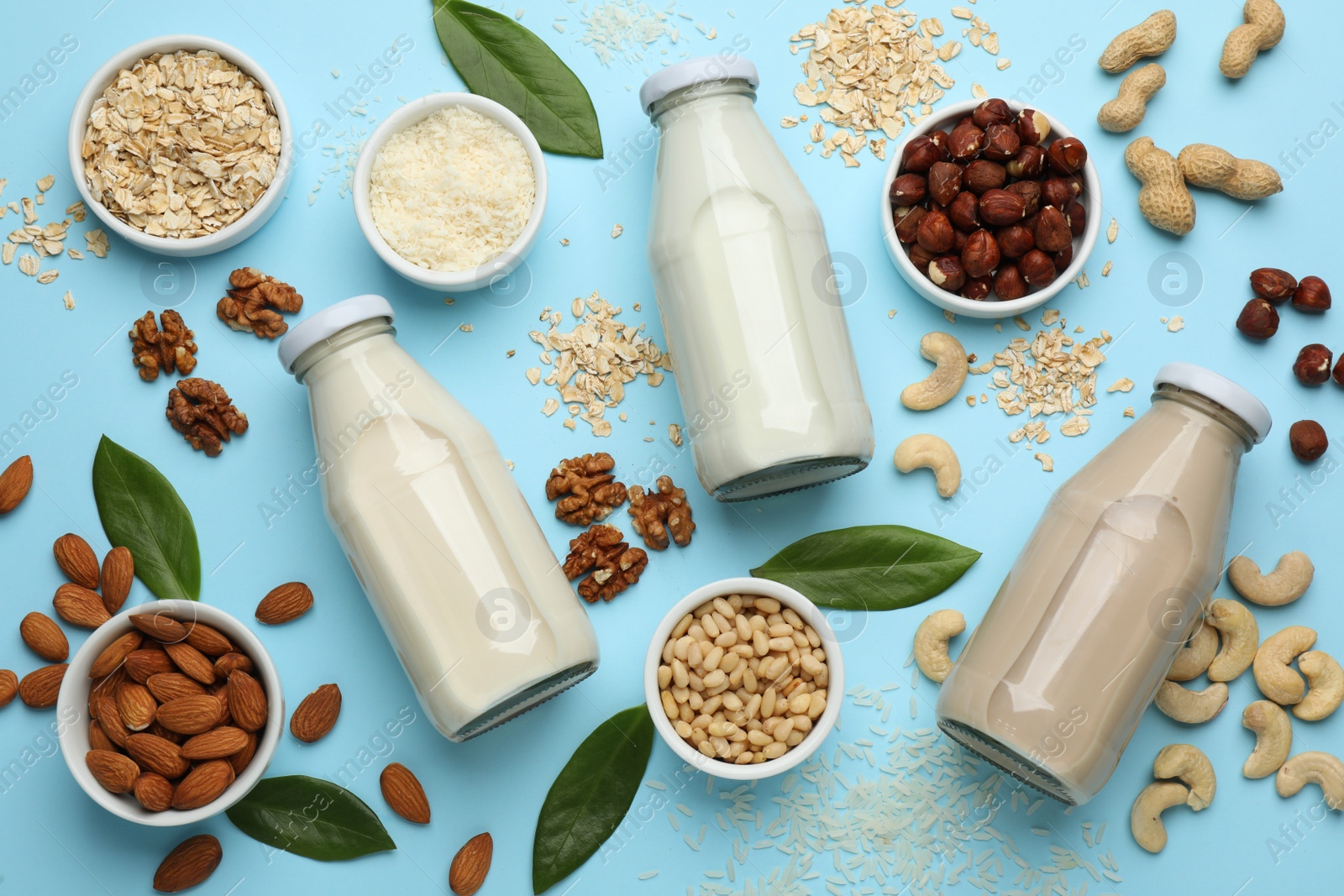 Photo of Different vegan milks and ingredients on light blue background, flat lay