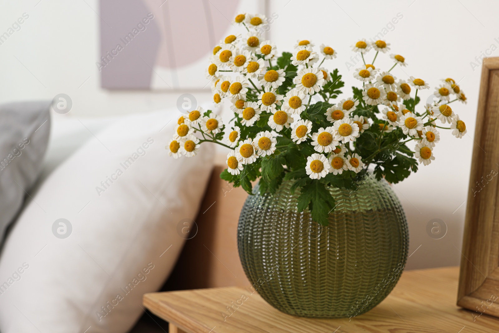 Photo of Beautiful bouquet of chamomile flowers on wooden nightstand in bedroom, space for text. Interior element