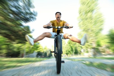 Image of Handsome young man riding bicycle in city park, low angle view. Motion blur effect