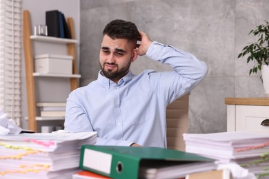 Overwhelmed man surrounded by documents at workplace in office