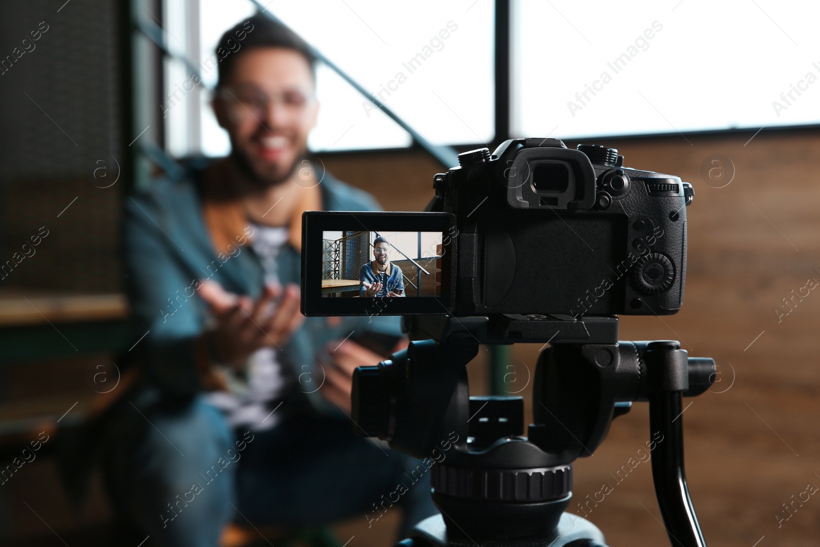 Photo of Young blogger recording video indoors, focus on camera screen