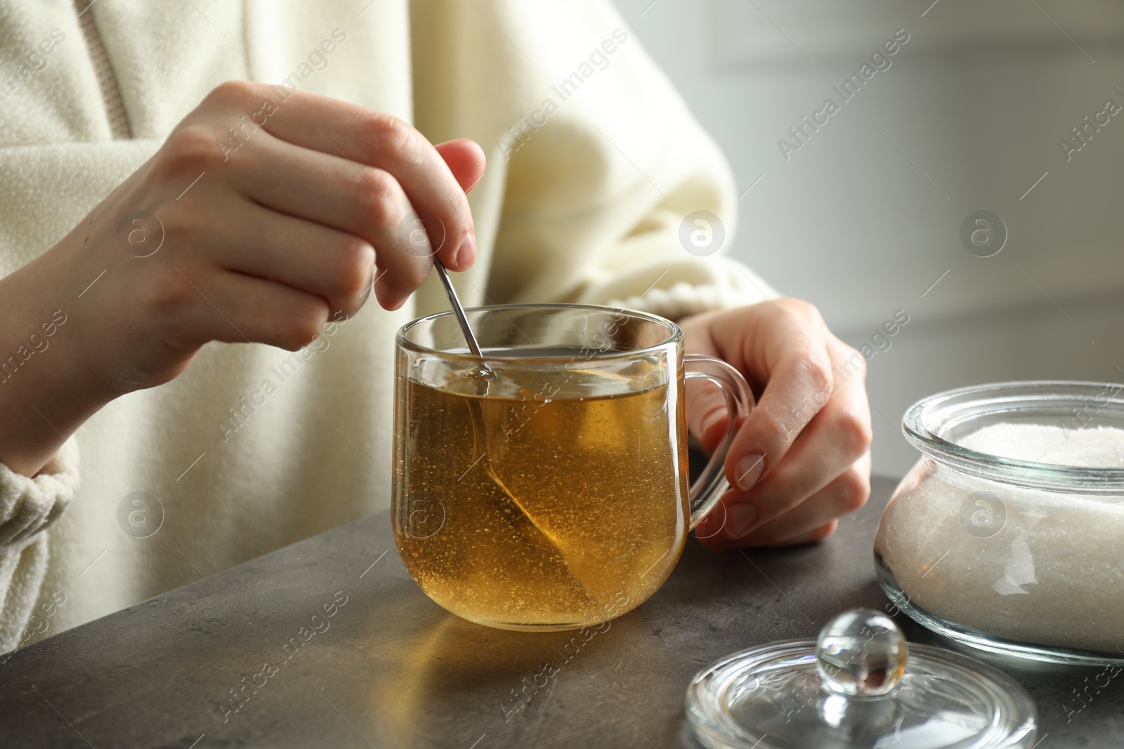 Photo of Woman stirring sugar in tea at grey table, closeup