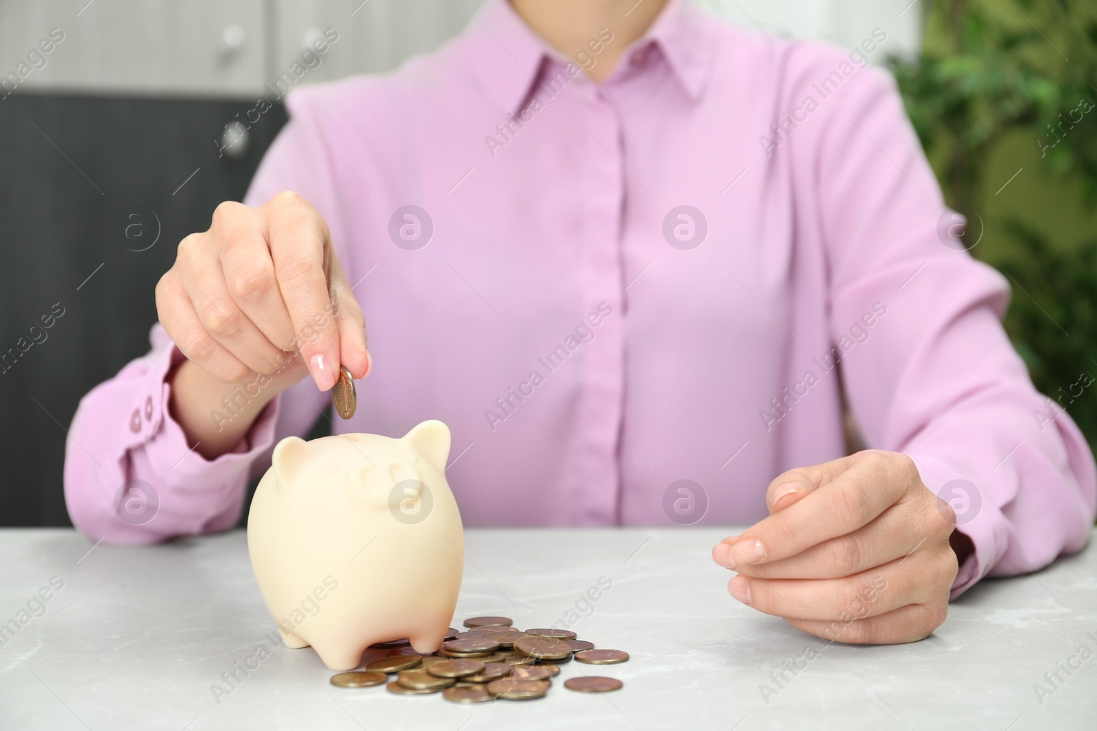 Photo of Woman putting coin into piggy bank at light table, closeup