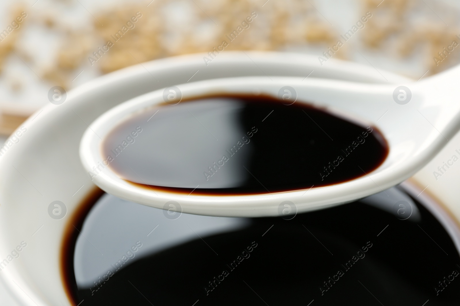 Photo of Spoon with soy sauce over bowl, closeup