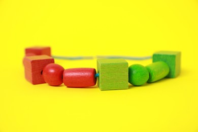 Wooden pieces and string for threading activity on yellow background, closeup. Educational toy for motor skills development