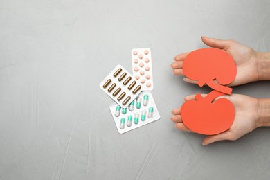 Woman holding paper cutout of kidneys near pills at grey table, top view. Space for text