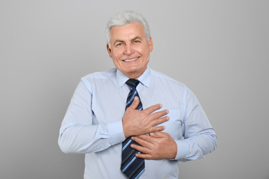 Grateful senior man with hands on chest against light grey background