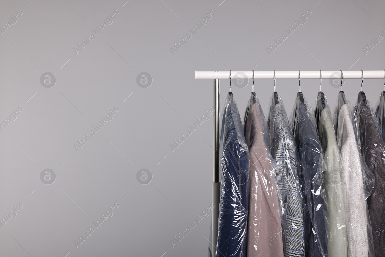 Photo of Dry-cleaning service. Many different clothes in plastic bags hanging on rack against grey background, space for text