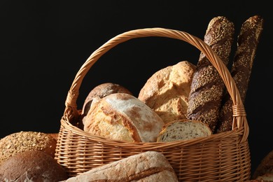 Photo of Wicker basket with different types of fresh bread against black background