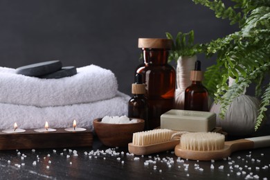 Spa composition. Brushes, soap bar, sea salt and burning candles on black table