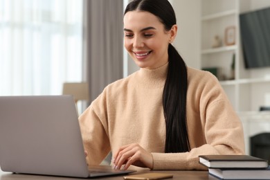 Photo of Happy woman working with laptop at wooden desk in room