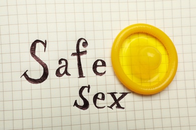 Photo of Yellow condom and words SAFE SEX on checkered paper, top view