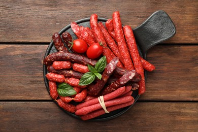 Photo of Different thin dry smoked sausages, basil and tomatoes on wooden table, top view