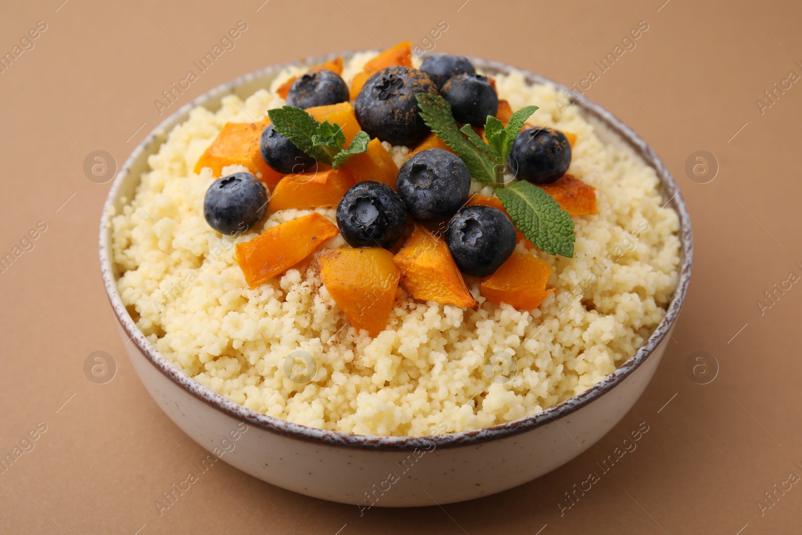 Photo of Bowl of tasty couscous with blueberries, pumpkin and mint on brown background, closeup