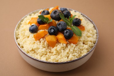 Bowl of tasty couscous with blueberries, pumpkin and mint on brown background, closeup