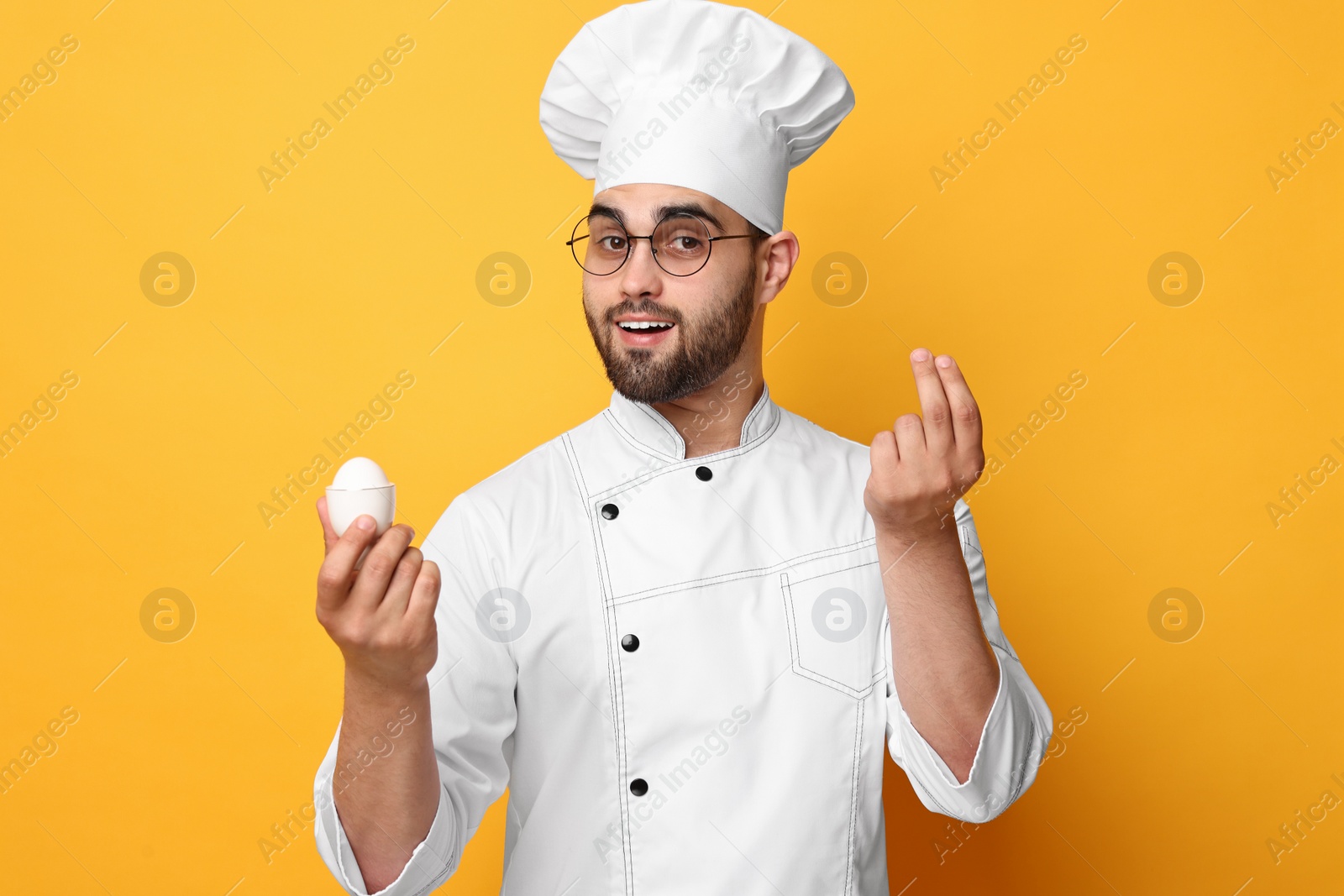 Photo of Professional chef holding egg and showing perfect sign on yellow background