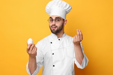 Photo of Professional chef holding egg and showing perfect sign on yellow background