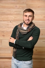 Photo of Handsome young man in warm sweater with scarf on wooden background