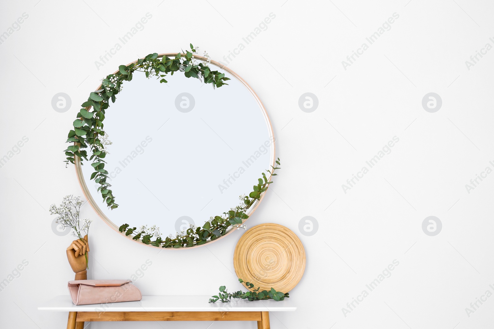 Photo of Round mirror and table with accessories near white wall. Modern interior design