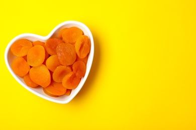 Photo of Bowl of dried apricots on color background, top view with space for text. Healthy fruit